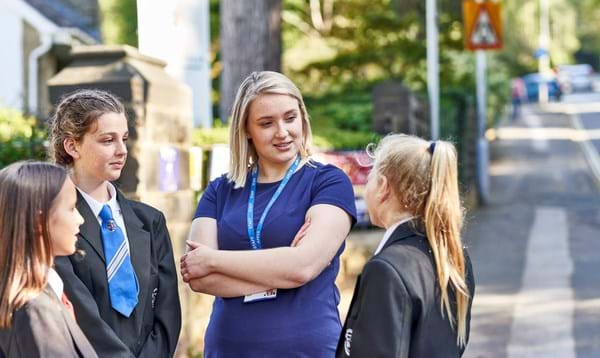 Female teacher speaks to 3 female pupils outside school gates