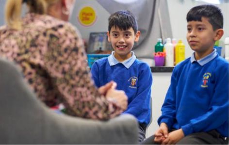 Two primary aged boys sitting, smiling and talking to a counsellor. They are all sitting in a Place2Be classroom.