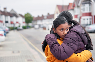 Two Asian girls hugging in the street, one looks sad or anxious