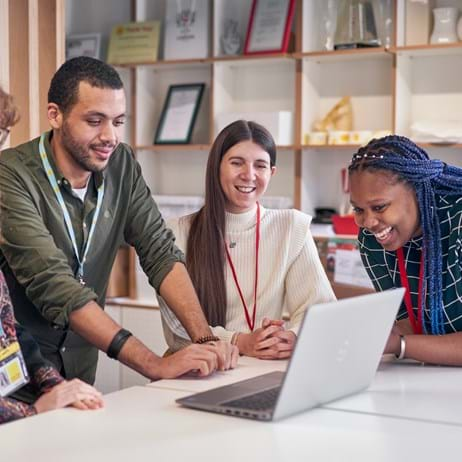 Diverse group of staff members gathered around a laptop