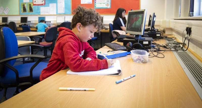 Boy sitting at desk writing on notepad