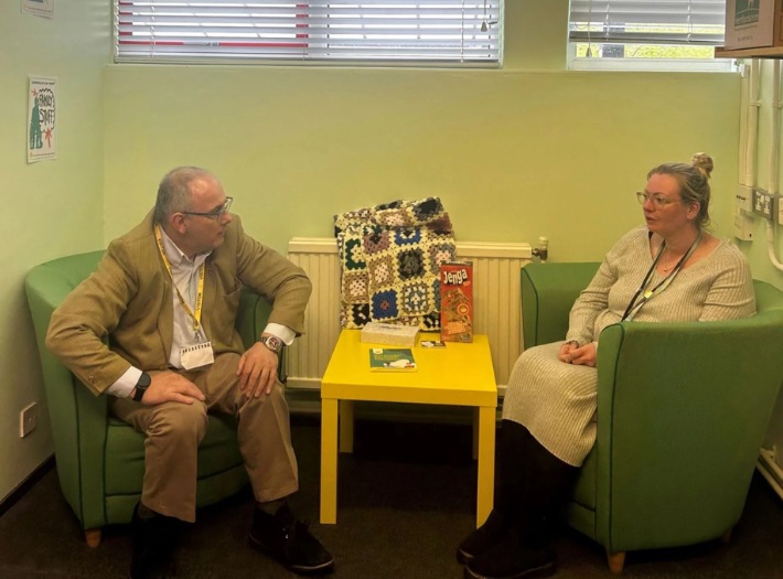 Harlow MP Rob Halfon speaking with a Place2Be School Project Manager. The pair are sitting on green armchairs inside a room with light green painted walls. 