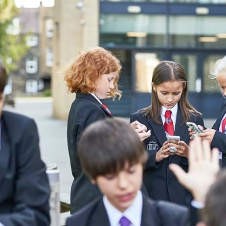 Young people in a school playground looking at mobile phones