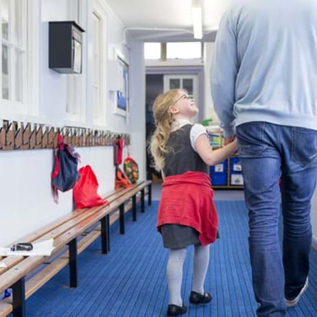 Little girl walking through her nursery corridor with her father. She is holding his hand and looking up to him with a smile on her face.