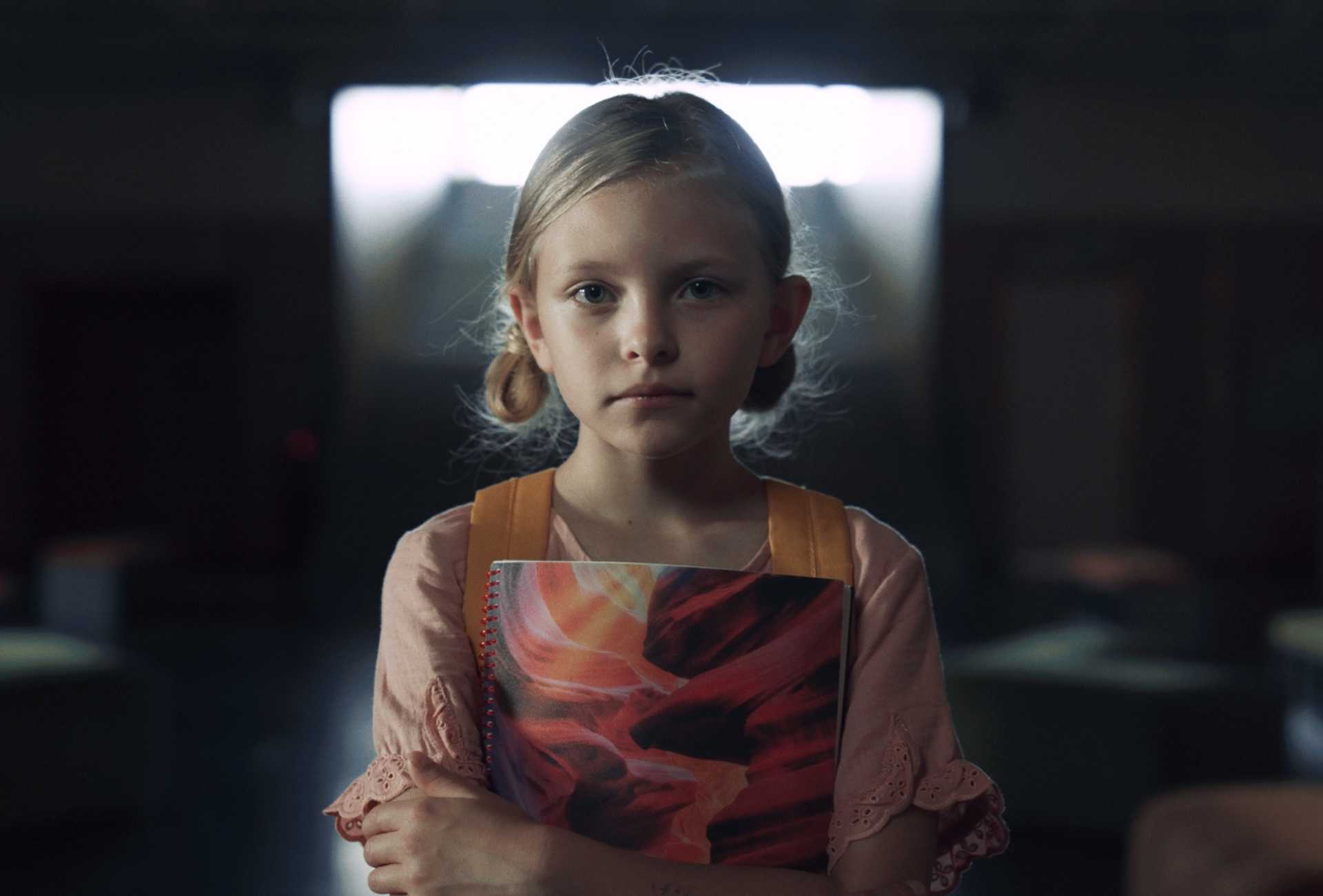 a young girl holding a book, with a blank expression in a dark room