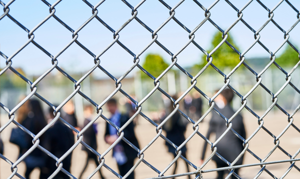 Secondary aged students in playground, out of focus, behind a wire fence