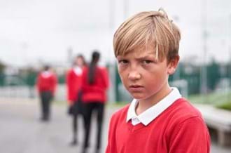 young boy in a red uniform looking sad in a school playground