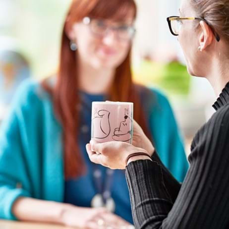 Two adults talking in a school, one holding a hot drink