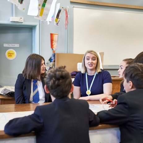 Teacher sitting with students at a desk looking at work