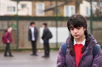 Young teenage girl stood alone in playground, looking sad