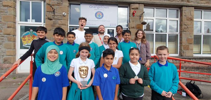 Pupils with presenters Joe Tasker and Shanequa Paris smiling at the camera. One pupil is holding the BAFTA Trophy.