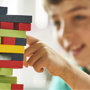 Boy at school playing Jenga with colourful blocks and smiling