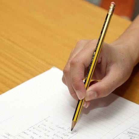 Person holding pencil against paper on desk