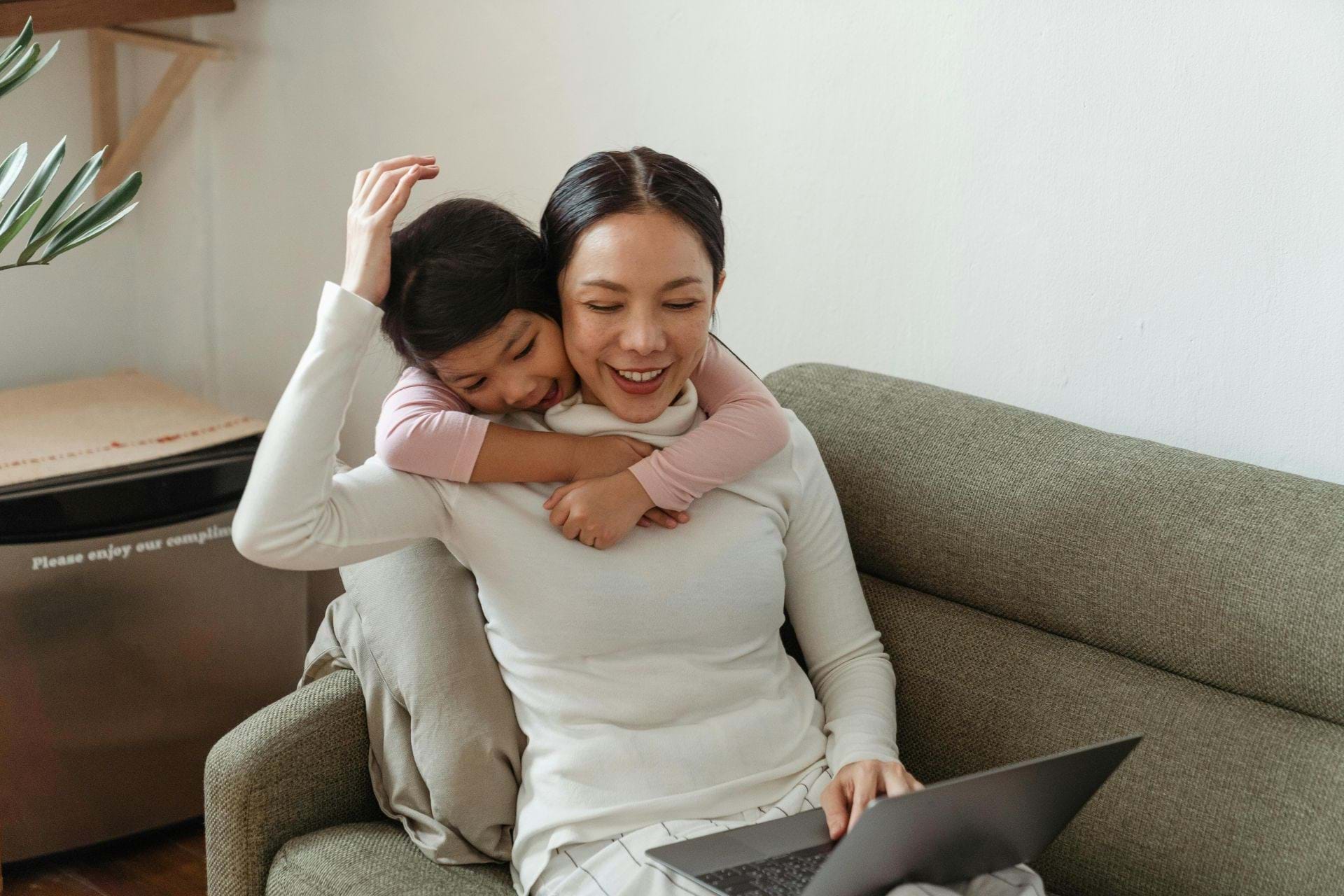 A parent and child looking at a laptop, the child is hugging the parent from behind.