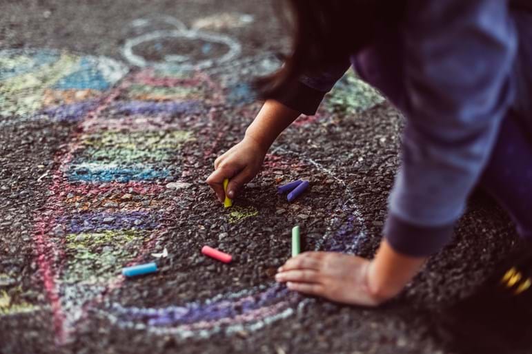 A pupil drawing a colourful picture of a butterfly in chalk on a concrete floor.
