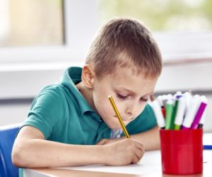 Young boy sitting at a desk writing with a pencil
