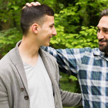 Father embracing son, both are outside in surrounded by trees