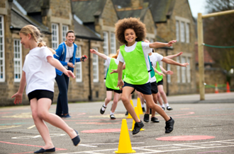 Children running in playground, one child in a green vest smiling at camera