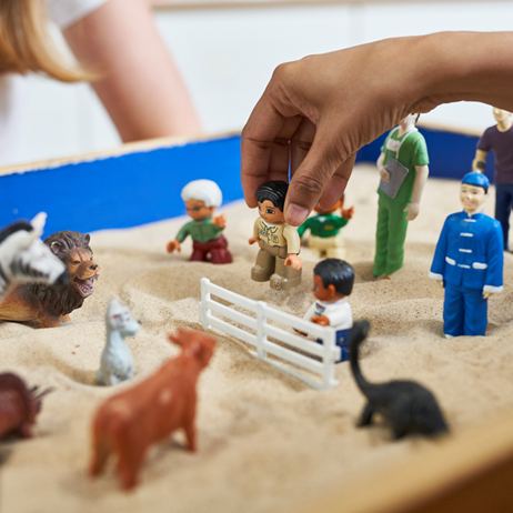 A hand playing with some toys in a sand pit