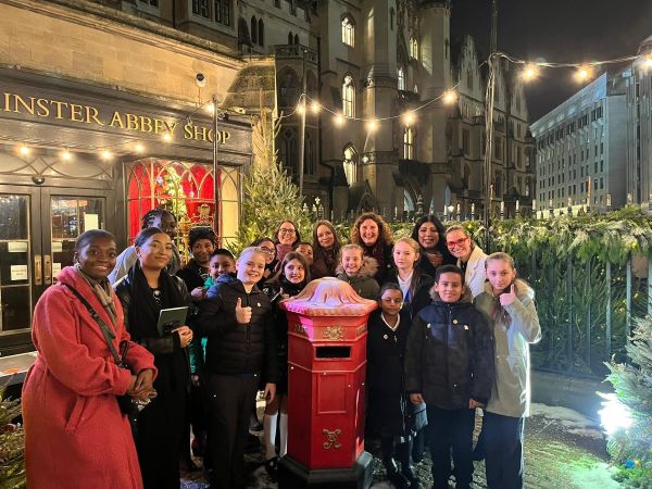 Place2Be colleagues with children and staff members from St. Johns Primary School. They are all standing around a red post box, outside the Westminster Abbey Shop.