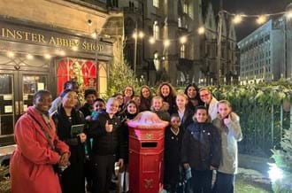 Place2Be colleagues with children and staff members from St. Johns Primary School. They are all standing around a red post box, outside the Westminster Abbey Shop.