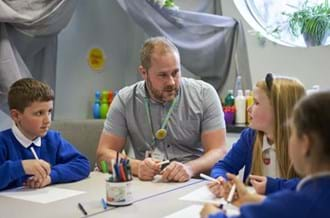 Male counsellor sitting down with three young children